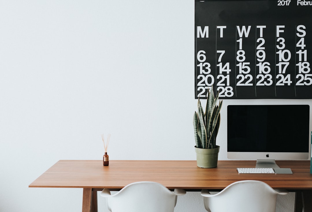 Large monthly wall calendar above a wooden desk with an iMac, illustrating monthly recurring revenue tracked period by period